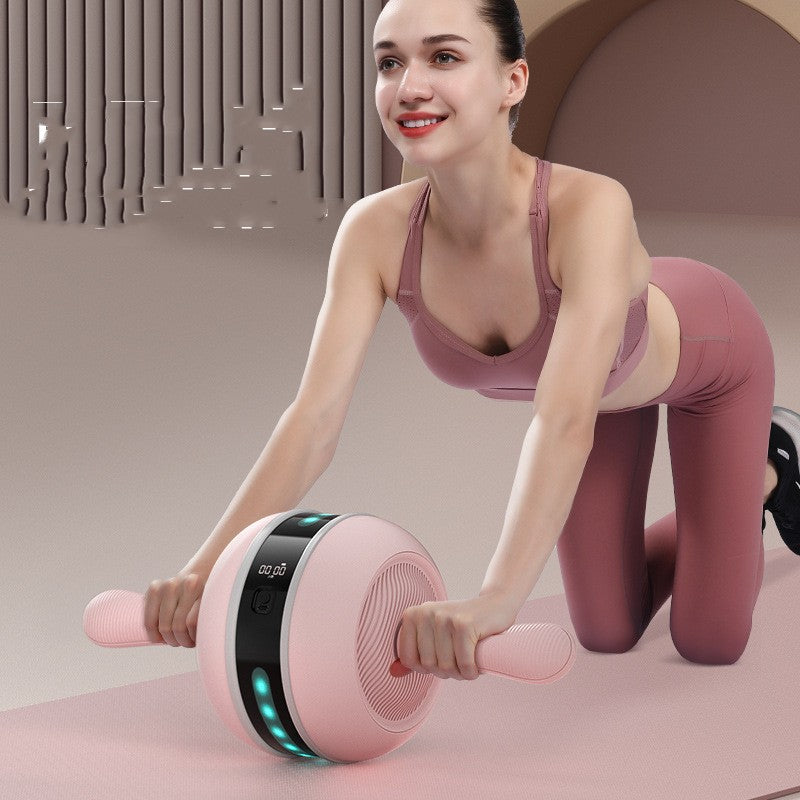 Woman in pink activewear uses Ab Wheel with LED light and USB charging, auto rep counter, on a pink mat.